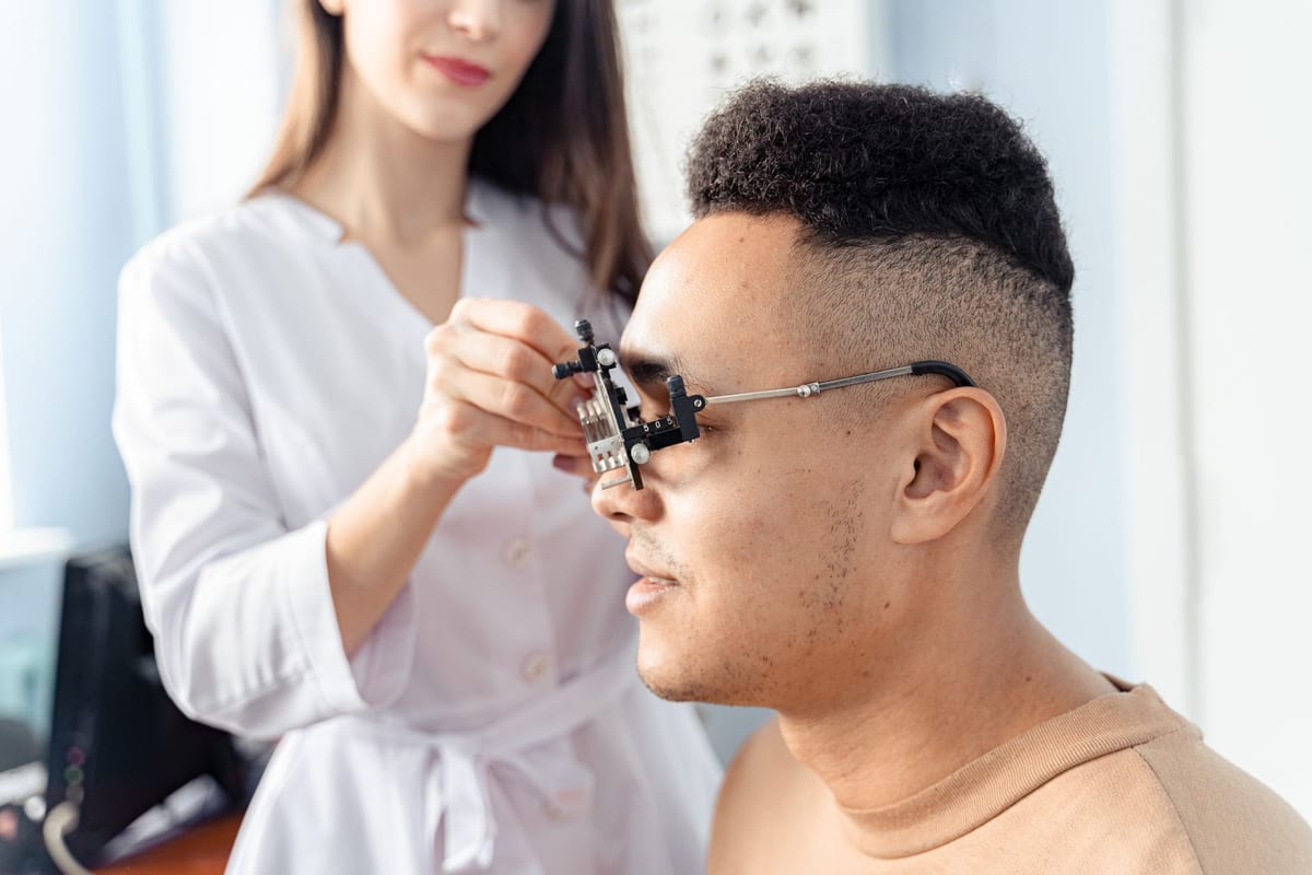 An optician holding a trial frame in front of a seated patient's eye during a vision test