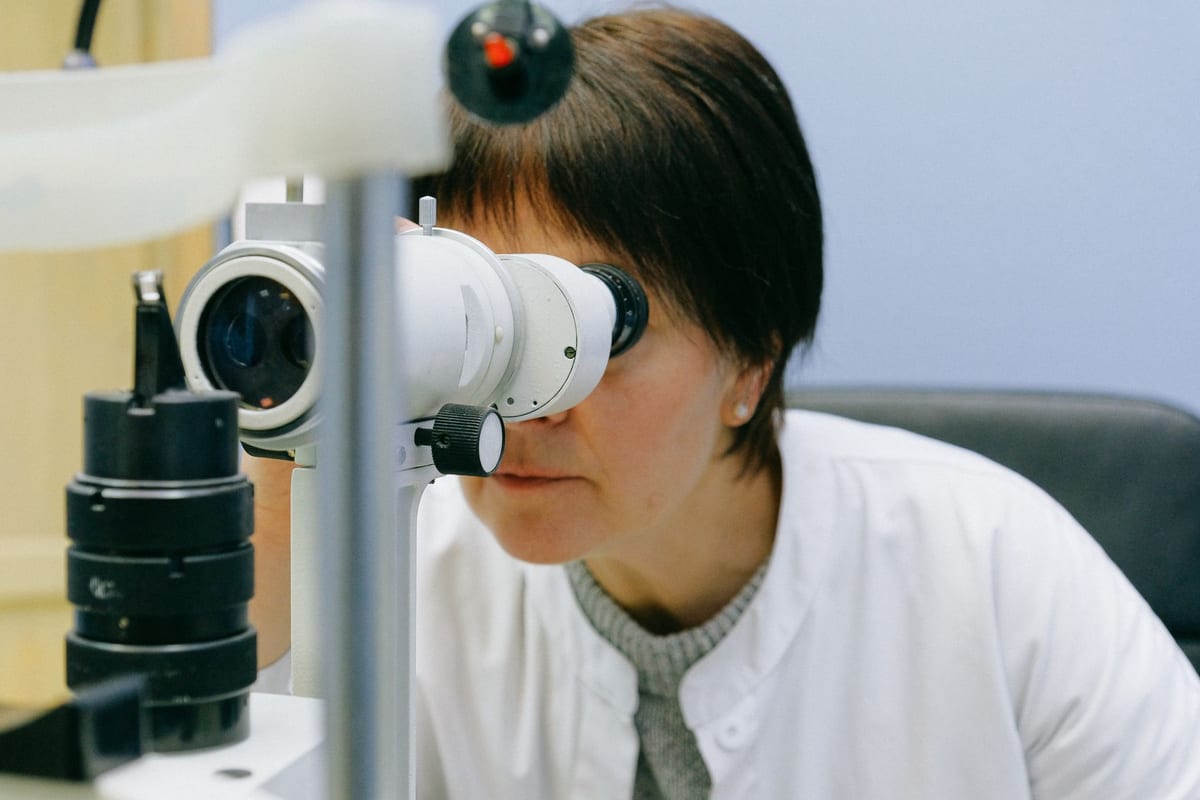A clinician examining a patient's eyes through the binocular eyepieces of a slit lamp