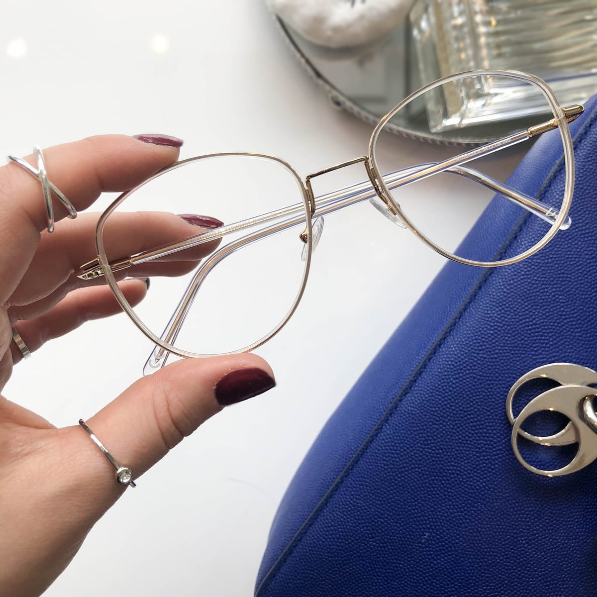 A hand holding a pair of clear and gold aviator frames in the studio